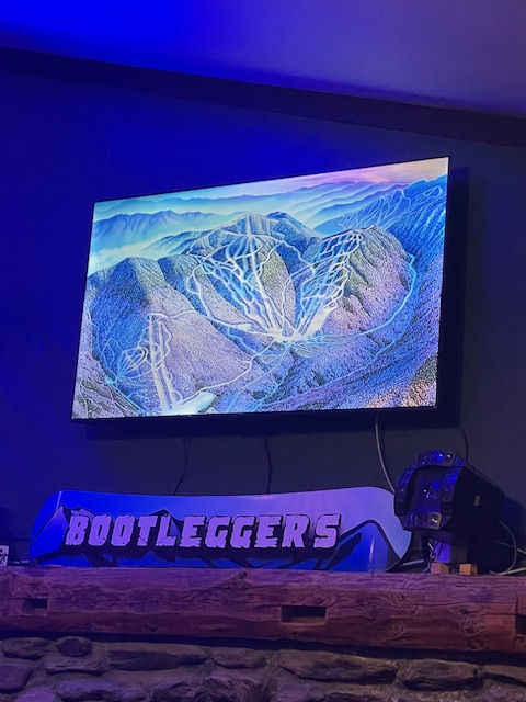 A television displaying a scenic aerial view of a mountainous landscape with winding roads and trails, set against a colorful sky.